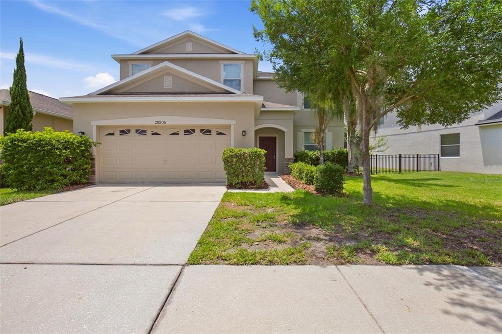 A two-story suburban house features a tan stucco exterior, a two-car garage, and landscaping — 20506 CAROLINA CHERRY COURT, TAMPA, FL