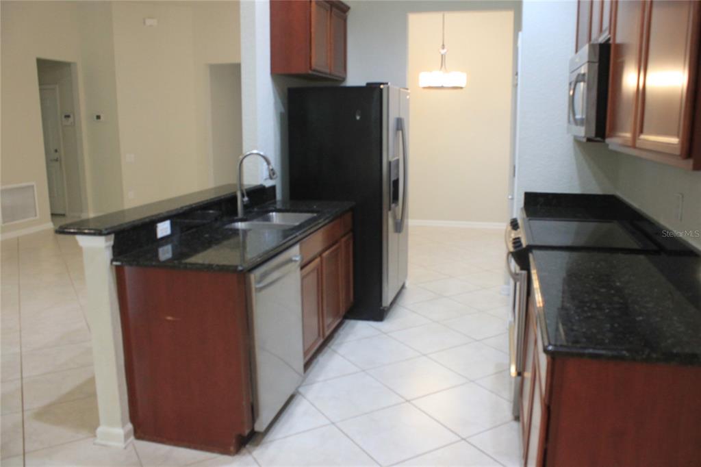 A kitchen features dark wood cabinets, black granite countertops, stainless steel appliances, and tile flooring — 7730 BROFIELD AVENUE, WINDERMERE, FL