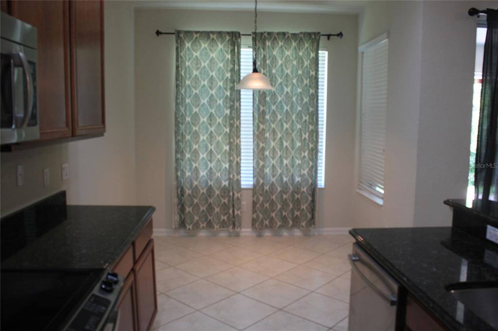 A kitchen with dark cabinets, granite countertops, tile flooring, and a dining area with curtains — 7730 BROFIELD AVENUE, WINDERMERE, FL