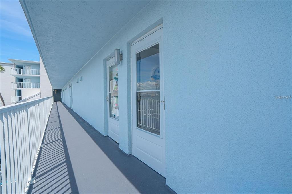 An exterior walkway with a white railing runs along a light blue building with doors — 3700 S ATLANTIC AVENUE UNIT 215, NEW SMYRNA BEACH, FL