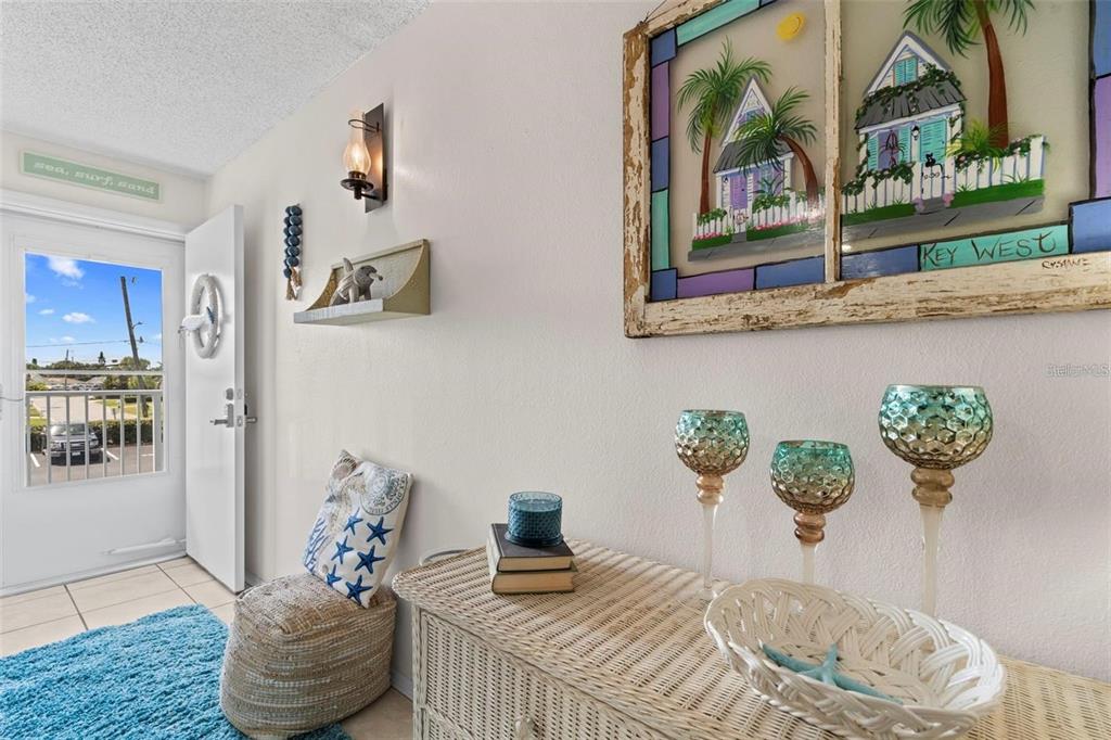 A coastal-themed entryway features a wicker console table, wall art, and a door to outside — 3700 S ATLANTIC AVENUE UNIT 215, NEW SMYRNA BEACH, FL