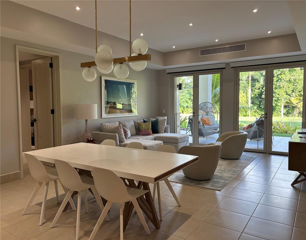 A dining area with a modern chandelier flows into a living room with glass doors — 7000 Bahia Beach Blvd LAS VERANDAS CONDOMINIUM UNIT 4128, RIO GRANDE, PR