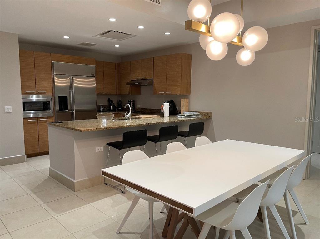 A modern kitchen with wood cabinets and a granite island flows into a dining area — 7000 Bahia Beach Blvd LAS VERANDAS CONDOMINIUM UNIT 4128, RIO GRANDE, PR