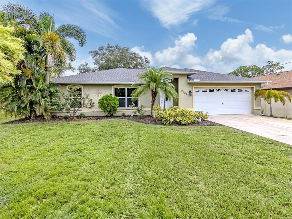 A single-story house with a white garage door, tan stucco exterior, and a front lawn — 2136 PENGUIN LANE, NORTH PORT, FL