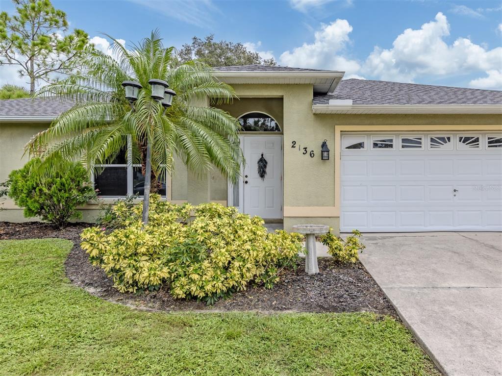 A single-story house exterior features a white front door, a garage, and a palm tree — 2136 PENGUIN LANE, NORTH PORT, FL