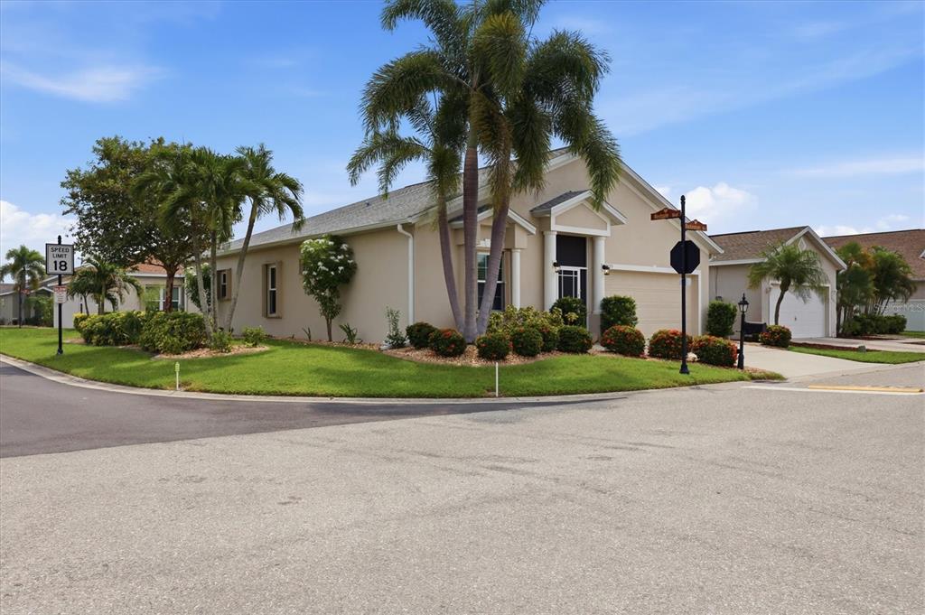 A tan single-story house with a palm tree and landscaping sits on a corner lot — 24195 BUCKINGHAM WAY, PORT CHARLOTTE, FL