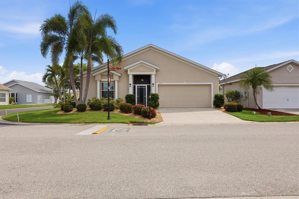 A single-story suburban house with a beige stucco exterior, a two-car garage, and palm trees — 24195 BUCKINGHAM WAY, PORT CHARLOTTE, FL