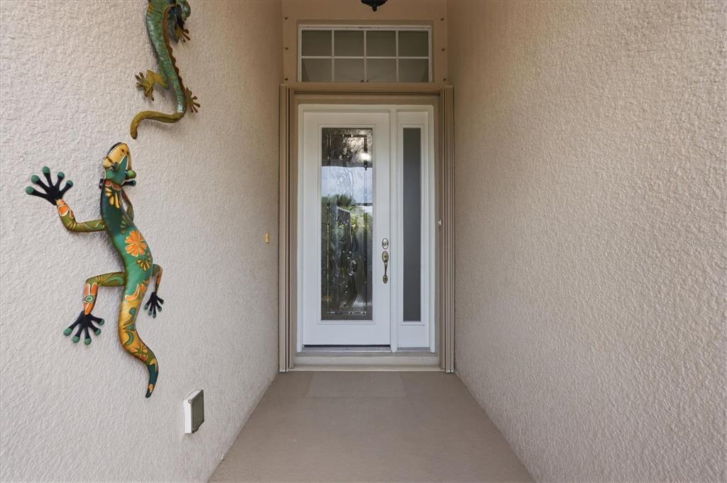 A front entryway features a white door with glass panels and two decorative metal lizards — 24195 BUCKINGHAM WAY, PORT CHARLOTTE, FL
