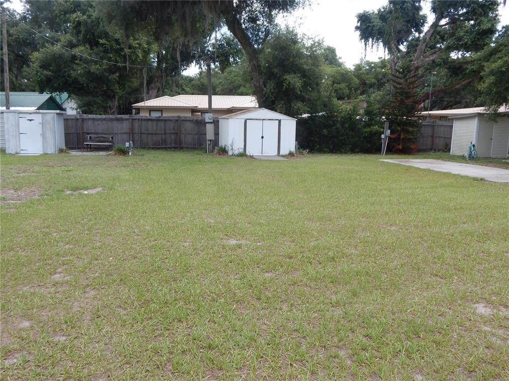 A grassy backyard features a wooden fence, three storage sheds, and mature trees — 18 ANCHOR INN ROAD, LAKE WALES, FL