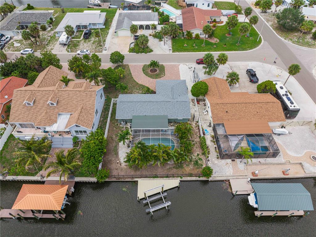 An aerial view shows three waterfront houses with pools, docks, and boat lifts along a canal — 1004 SPINDLE PALM WAY, APOLLO BEACH, FL