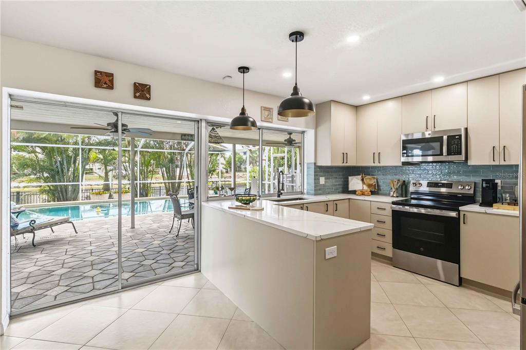 A kitchen with light cabinets, a quartz island, and a sliding door opening to a pool — 1004 SPINDLE PALM WAY, APOLLO BEACH, FL