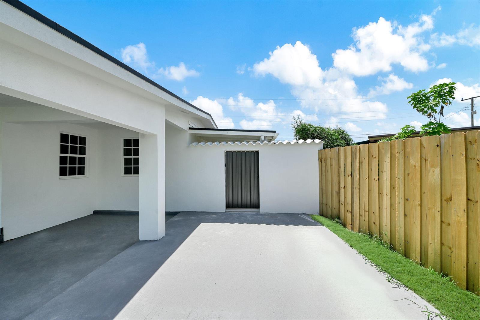 A white house exterior features a covered carport, a side gate, and a wooden fence — 4040 SW 108th Avenue, Miami FL 33165, MIAMI, FL