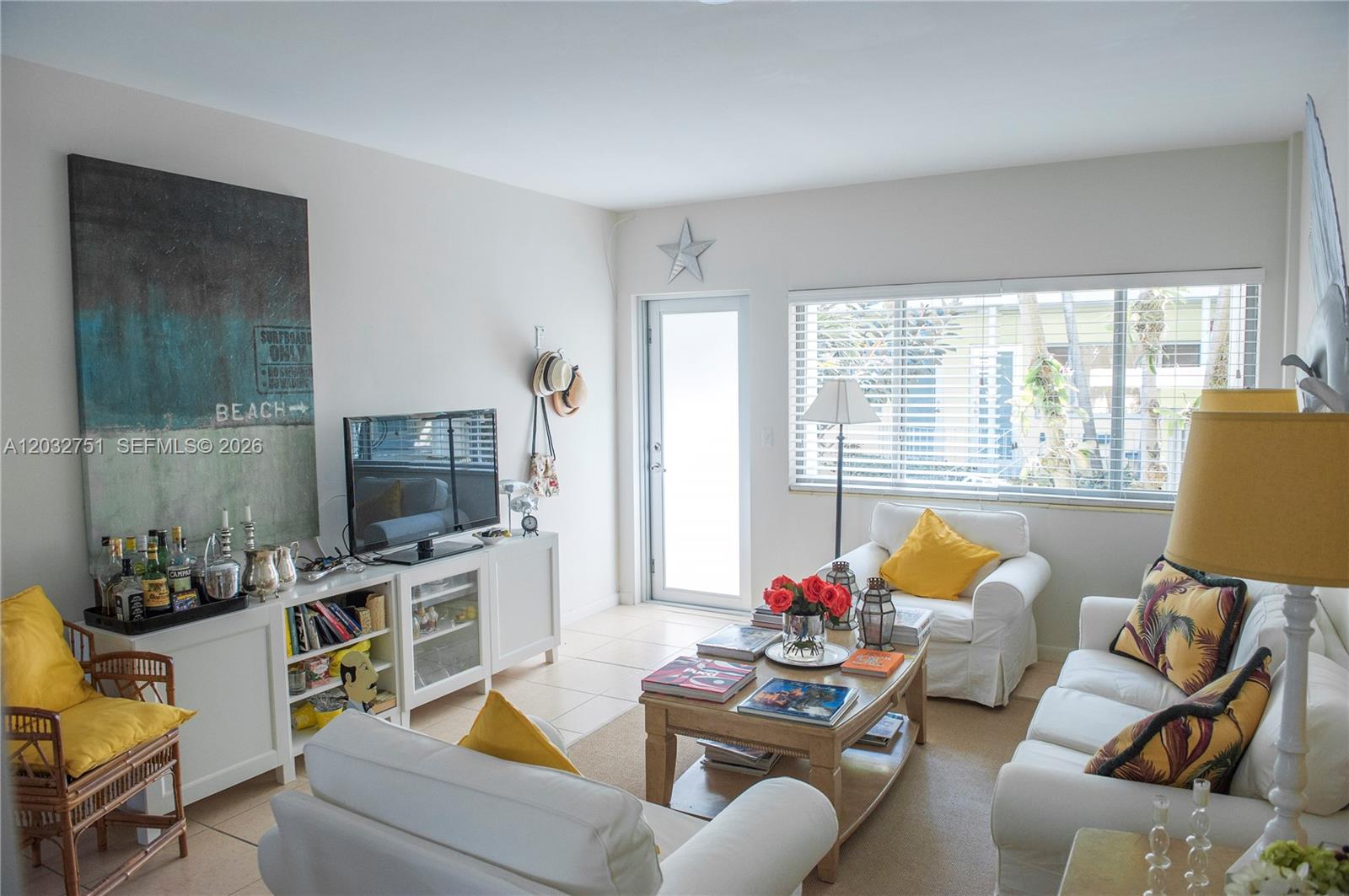A bright living room features white furniture, a coffee table, and a large beach-themed wall art — 1840 James Ave # 10, Miami Beach FL 33139, MIAMI BEACH, FL