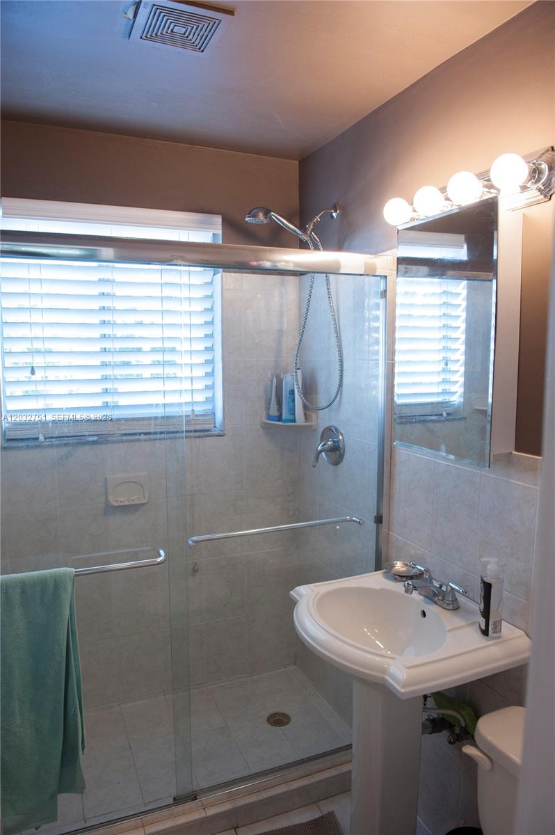 A bathroom features a glass-enclosed shower, a pedestal sink, and a mirrored medicine cabinet — 1840 James Ave # 10, Miami Beach FL 33139, MIAMI BEACH, FL