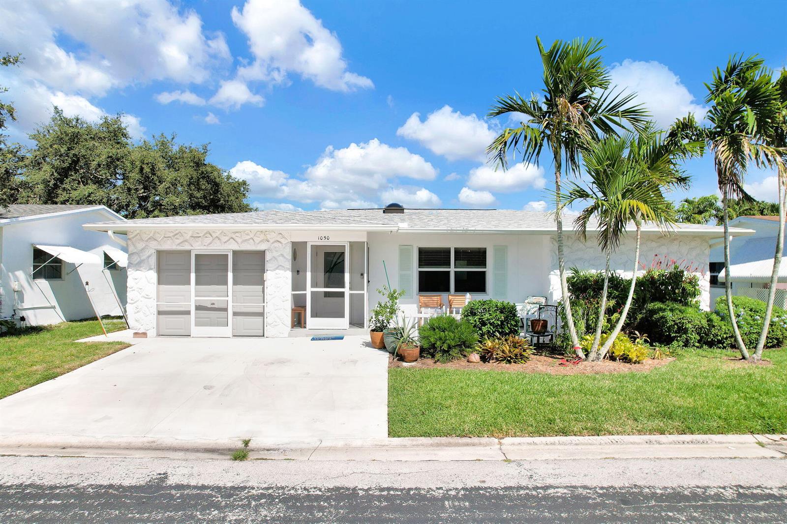 A white single-story house with a concrete driveway, palm trees, and a front lawn — 1050 NW 73rd Terrace, Margate FL 33063, MARGATE, FL
