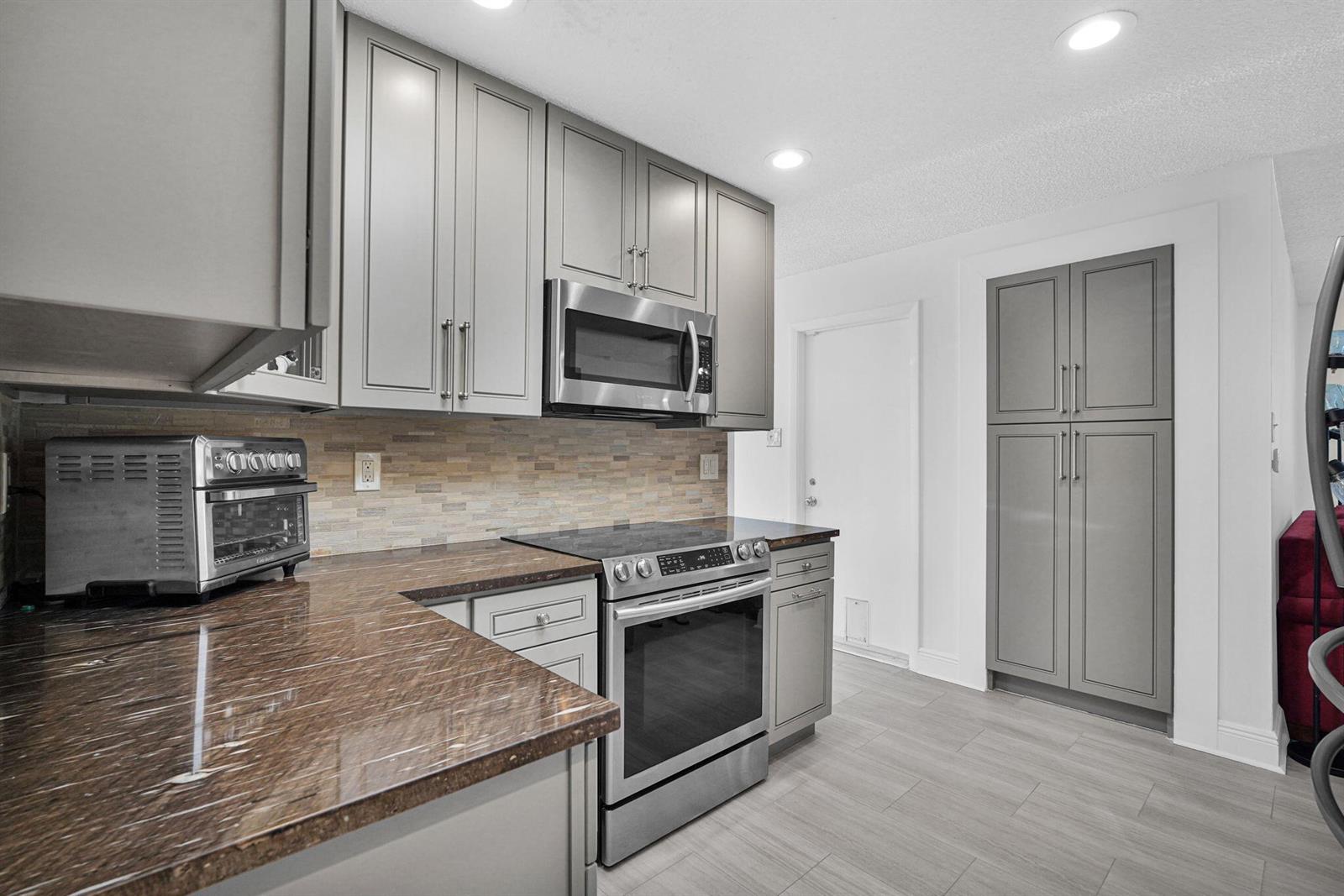 A kitchen features gray cabinets, brown granite countertops, stainless steel appliances, and tile flooring — 1050 NW 73rd Terrace, Margate FL 33063, MARGATE, FL