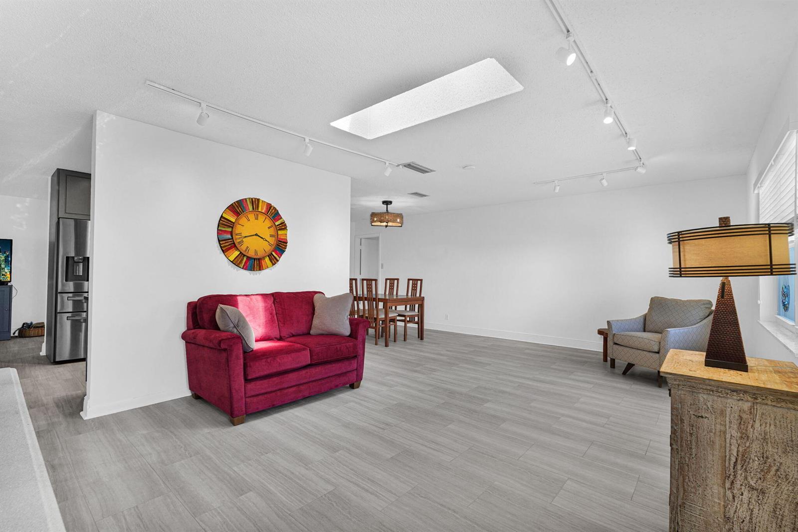 A living room with gray wood-look flooring, a red sofa, and a colorful wall clock — 1050 NW 73rd Terrace, Margate FL 33063, MARGATE, FL