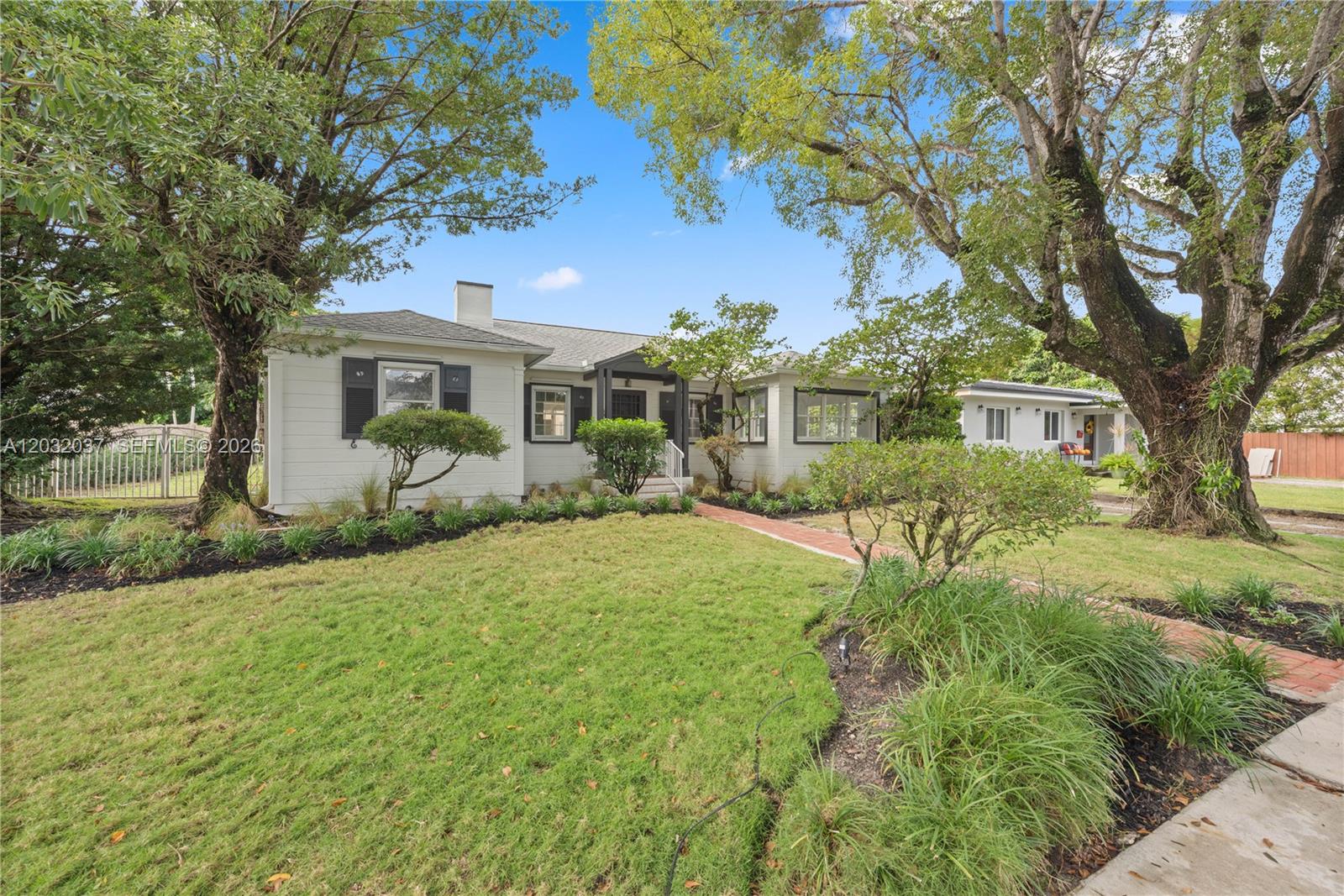 A single-story white house with dark shutters sits behind a lawn and mature trees — 440 SW 29th Rd, Miami FL 33129, MIAMI, FL