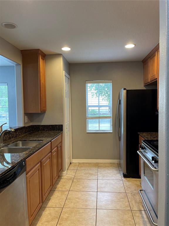 A kitchen features wood cabinets, granite countertops, stainless steel appliances, and beige tile flooring — 12910 JESSUP WATCH PLACE, RIVERVIEW, FL