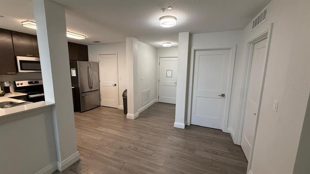 A kitchen with dark cabinets and stainless steel appliances opens into a hallway with doors — 14501 GROVE RESORT AVENUE UNIT 3429, WINTER GARDEN, FL