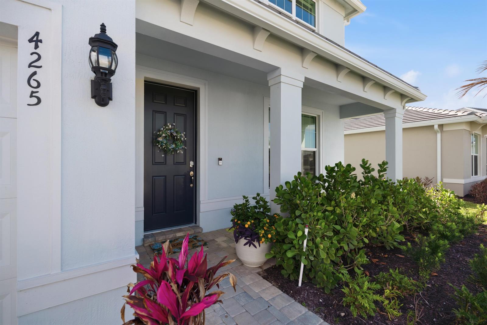 The exterior of a light blue house features a dark front door and paved walkway — 4265 SW Cornerstone Way, Stuart FL 34997, STUART, FL