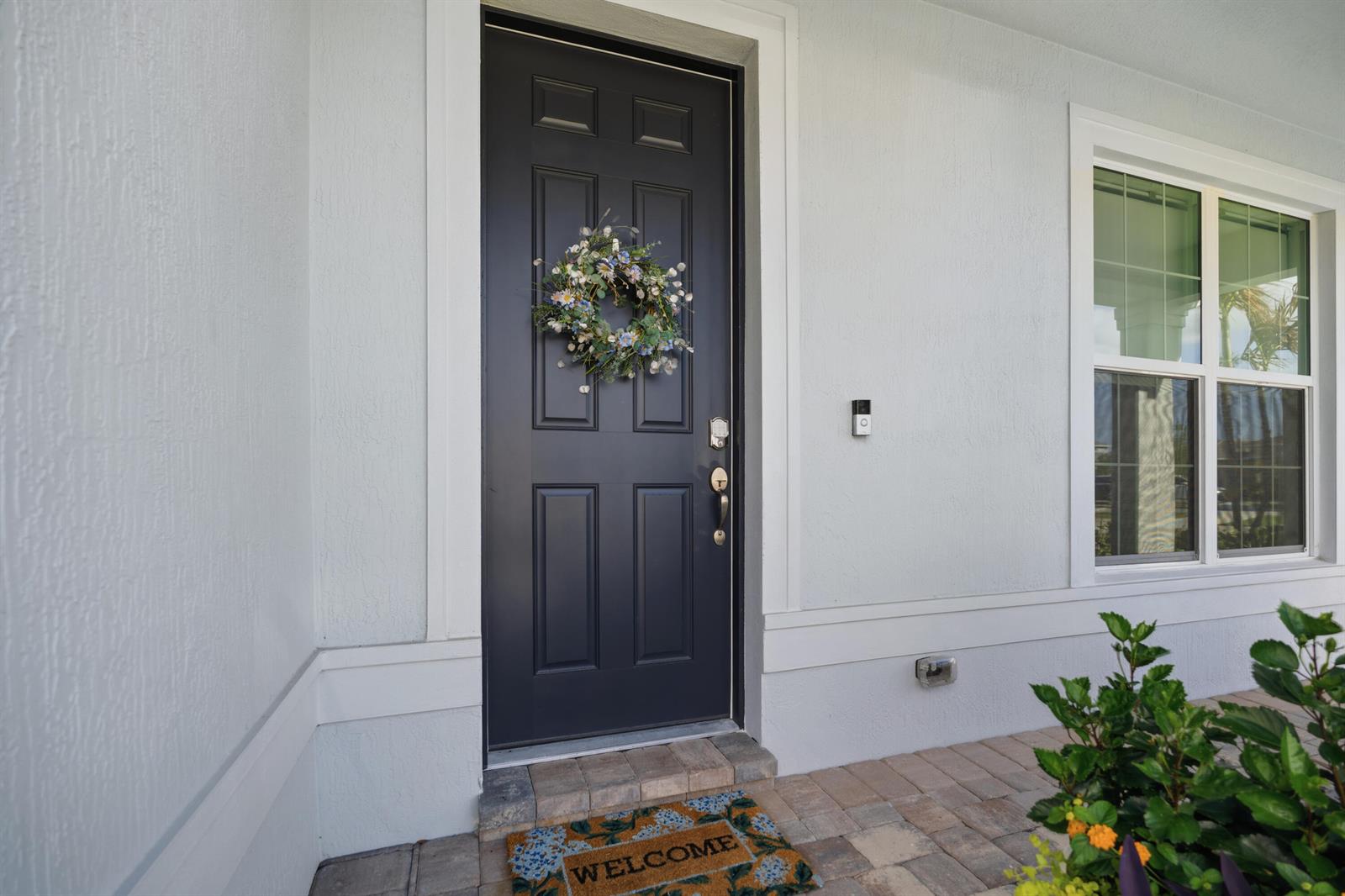 A dark front door with a floral wreath and a welcome mat on a porch — 4265 SW Cornerstone Way, Stuart FL 34997, STUART, FL