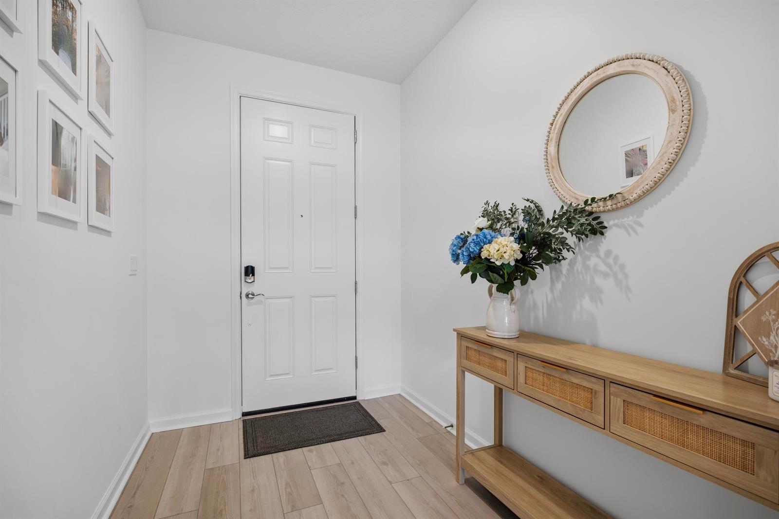 A bright entryway features light wood flooring, a console table, a round mirror, and wall art — 4265 SW Cornerstone Way, Stuart FL 34997, STUART, FL