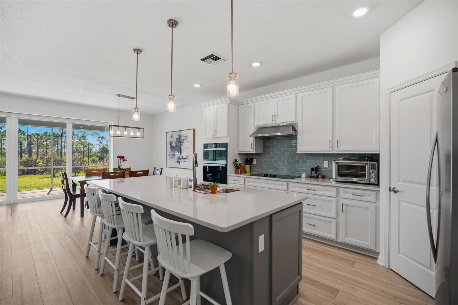 A modern kitchen features a gray island, white cabinetry, and a view of the backyard — 4265 SW Cornerstone Way, Stuart FL 34997, STUART, FL