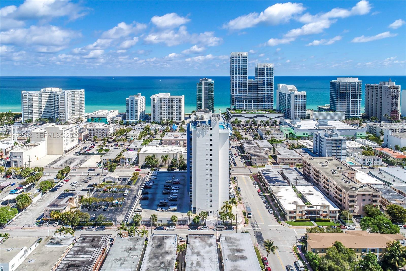 An aerial view shows a tall white apartment building surrounded by city streets and parking lots — 401 69 ST # 411, Miami Beach FL 33141, MIAMI BEACH, FL