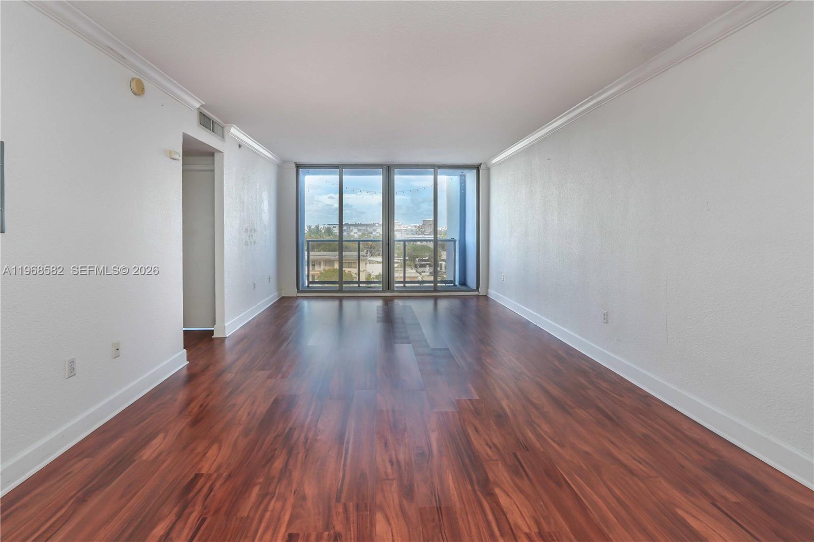 An empty room with dark wood flooring, white walls, and a sliding glass balcony door — 401 69 ST # 411, Miami Beach FL 33141, MIAMI BEACH, FL