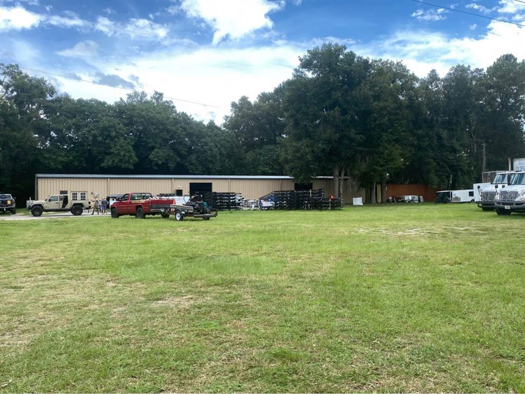 A large metal warehouse building sits behind a grassy field with several parked vehicles — 7800 SE 129TH PLACE, SUMMERFIELD, FL