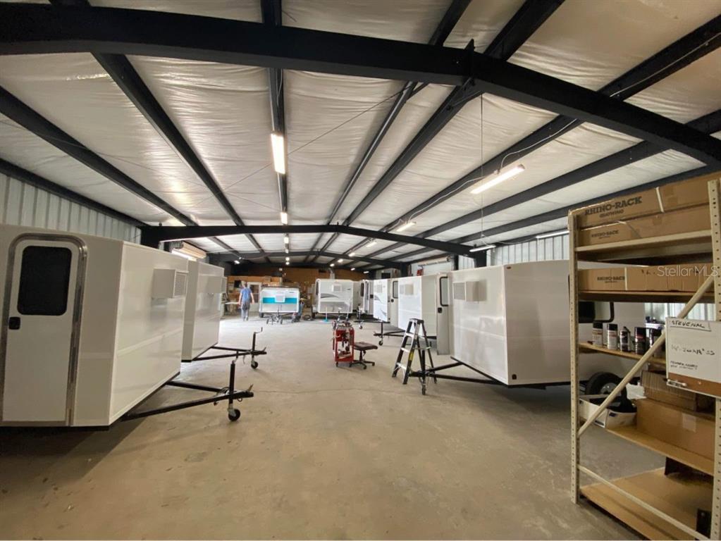 A large warehouse interior features multiple small white trailers parked on a concrete floor — 7800 SE 129TH PLACE, SUMMERFIELD, FL