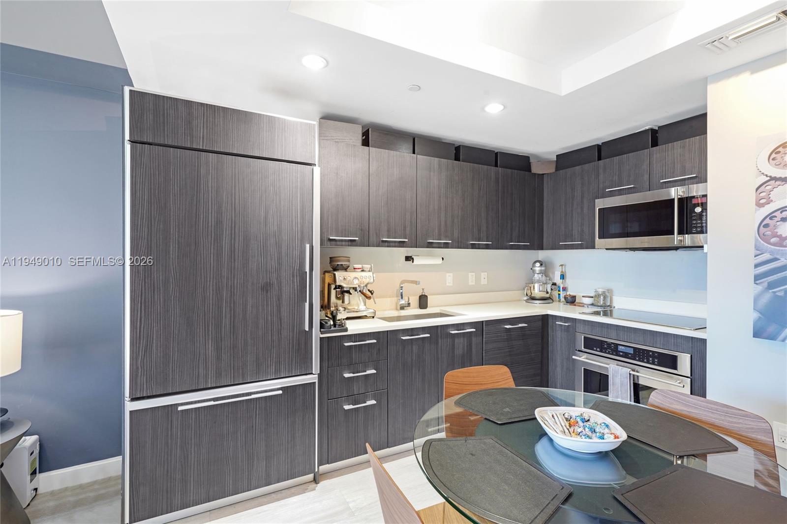 A modern kitchen features dark wood-grain cabinetry, stainless steel appliances, and a glass dining table — 45 SW 9th St # 3405, Miami FL 33130, MIAMI, FL