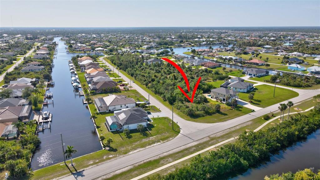 An aerial view shows a vacant, brush-covered residential lot situated between two houses and canals — 15645 SEAFOAM CIRCLE, PORT CHARLOTTE, FL