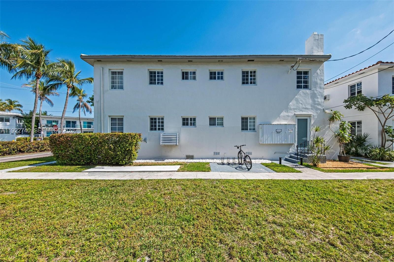 A two-story white apartment building features multiple windows, a bike rack, and palm trees — 7124 Bay Dr, Miami Beach FL 33141, MIAMI BEACH, FL