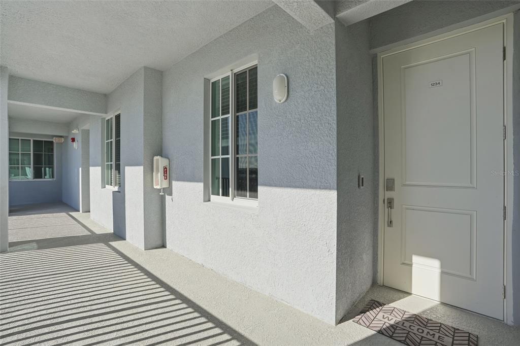 A view of a light-colored apartment building exterior hallway with a white entrance door — 14191 HERITAGE LANDING BOULEVARD UNIT 1234, PUNTA GORDA, FL