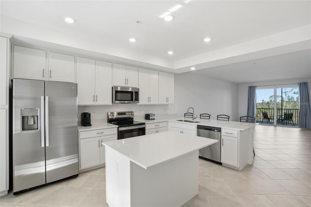 A modern kitchen features white cabinetry, stainless steel appliances, a center island, and tile flooring — 14191 HERITAGE LANDING BOULEVARD UNIT 1234, PUNTA GORDA, FL