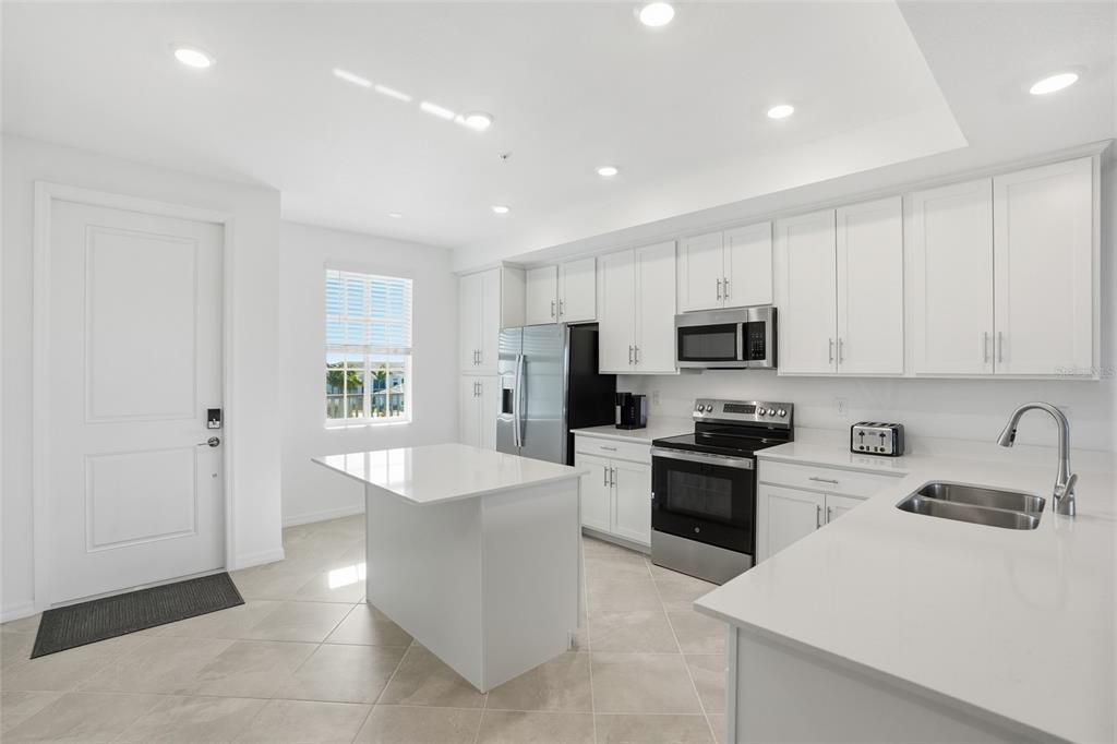 A modern kitchen features white cabinetry, stainless steel appliances, a center island, and tile flooring — 14191 HERITAGE LANDING BOULEVARD UNIT 1234, PUNTA GORDA, FL