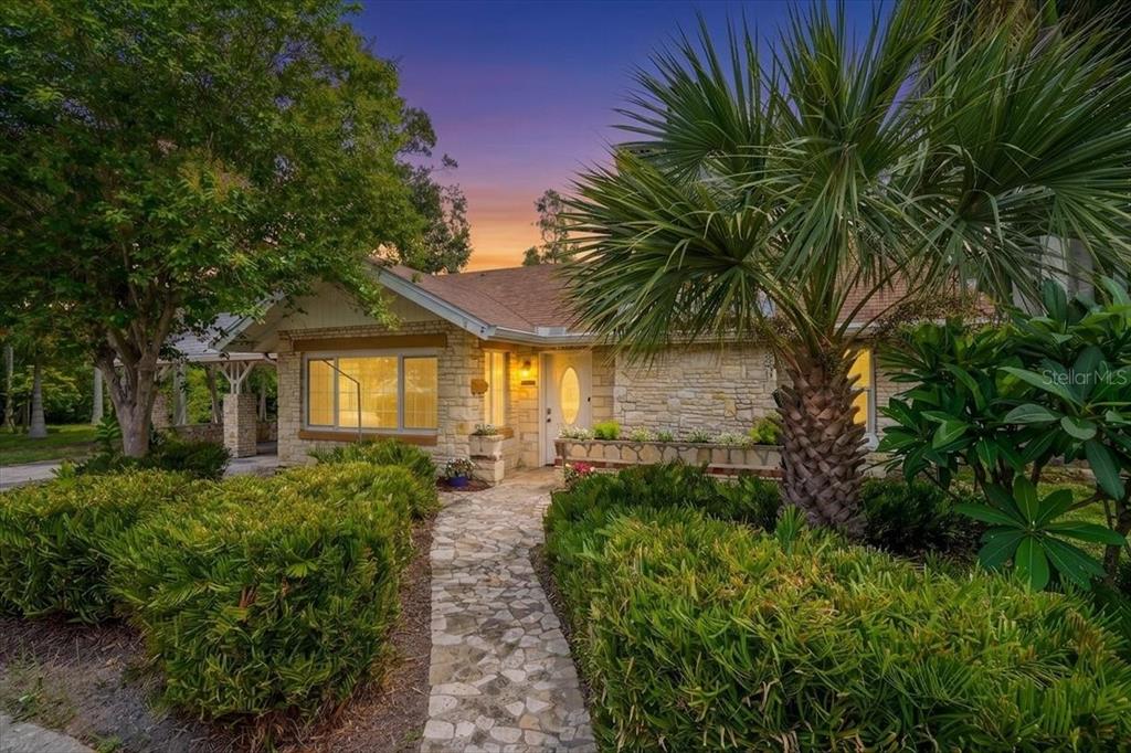 A stone-faced house with a stone walkway, lush landscaping, and a palm tree at sunset — 1830 9TH AVENUE W, BRADENTON, FL