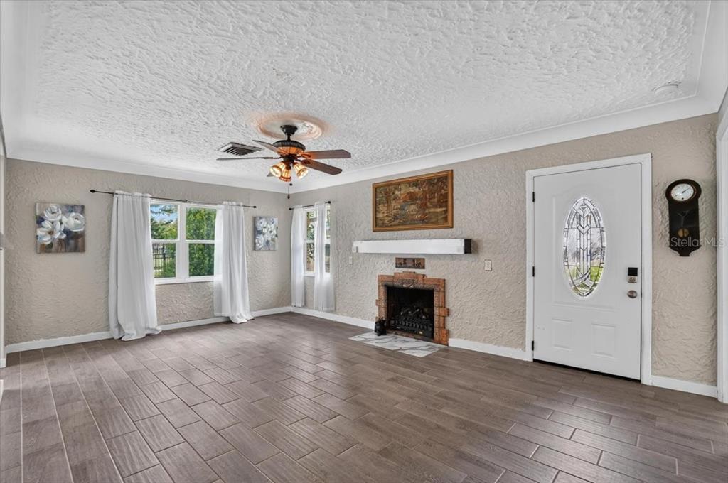 A living room features wood-look tile flooring, a fireplace, a ceiling fan, and a front door — 1830 9TH AVENUE W, BRADENTON, FL