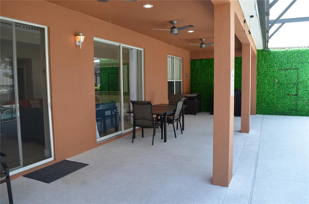 A covered patio features a dining set, ceiling fans, and artificial green wall panels — 8667 LA ISLA DRIVE, KISSIMMEE, FL
