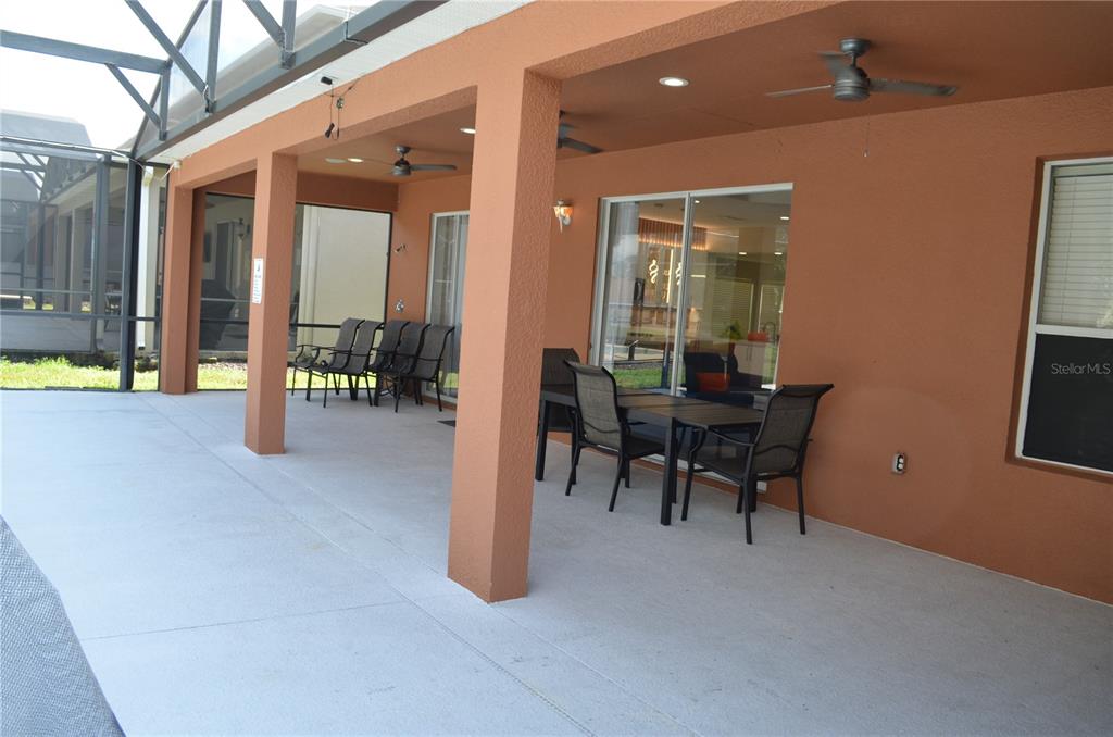 A covered patio features a concrete floor, outdoor furniture, ceiling fans, and sliding glass doors — 8667 LA ISLA DRIVE, KISSIMMEE, FL