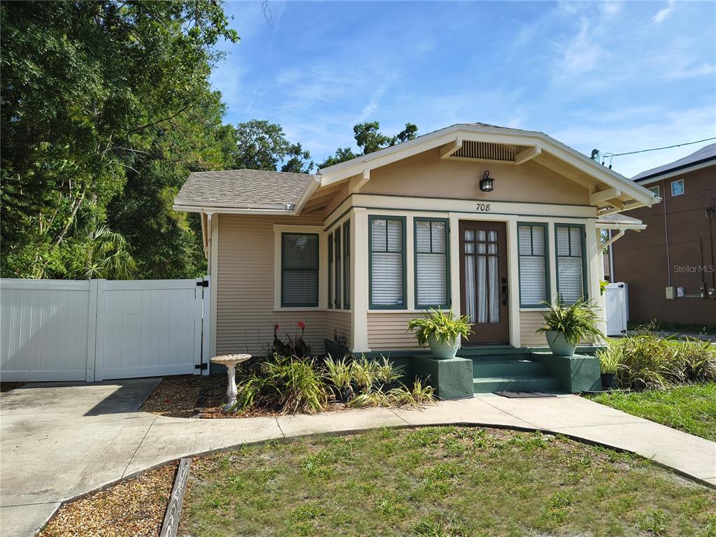 A tan bungalow with a front porch, green trim, and a white vinyl fence — 708 W IDLEWILD AVENUE, TAMPA, FL