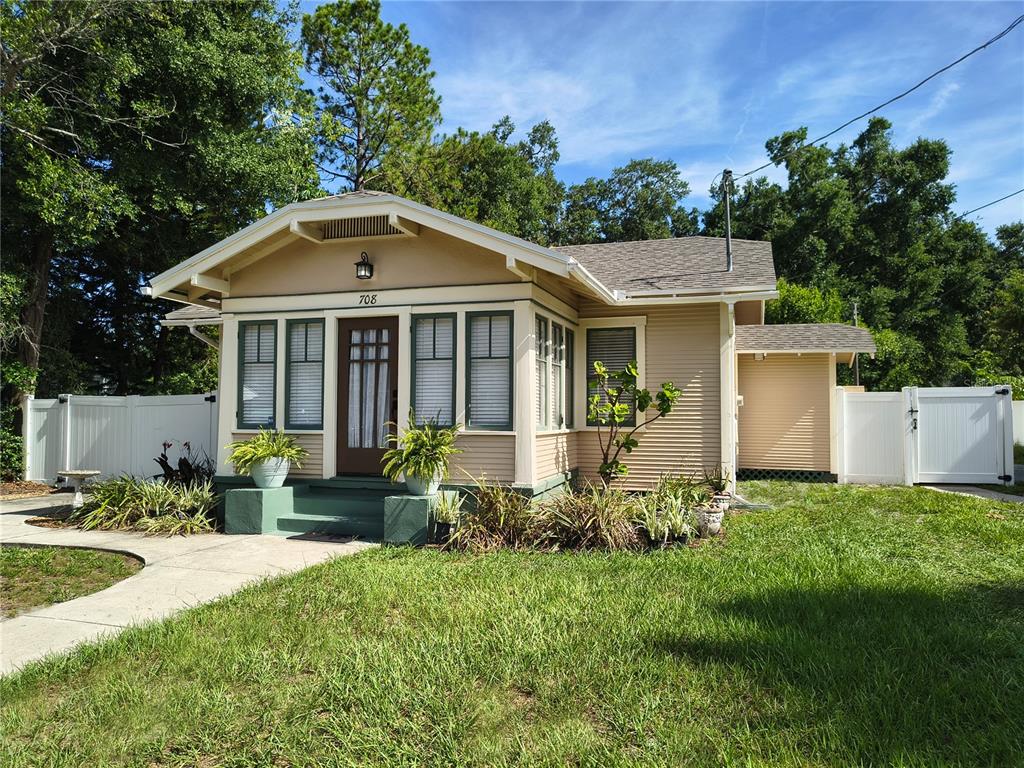 A tan bungalow with a front porch, dark trim, and a white vinyl fence — 708 W IDLEWILD AVENUE, TAMPA, FL