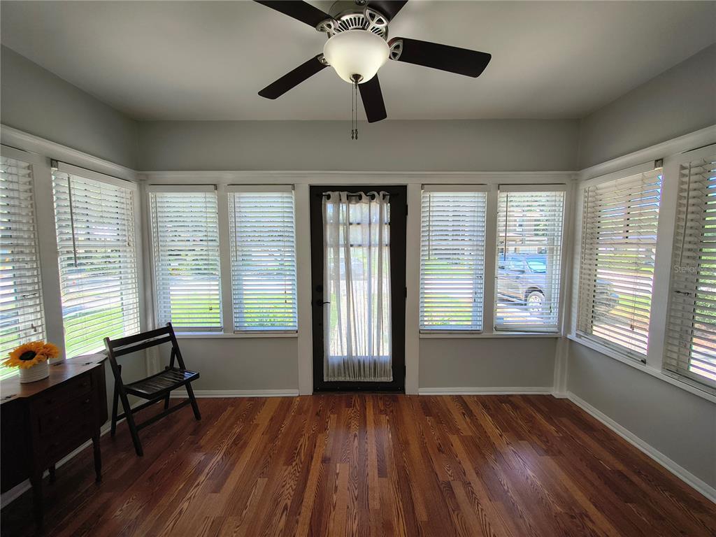 A sunroom with hardwood floors, a ceiling fan, and multiple windows flanking a glass-paneled door — 708 W IDLEWILD AVENUE, TAMPA, FL
