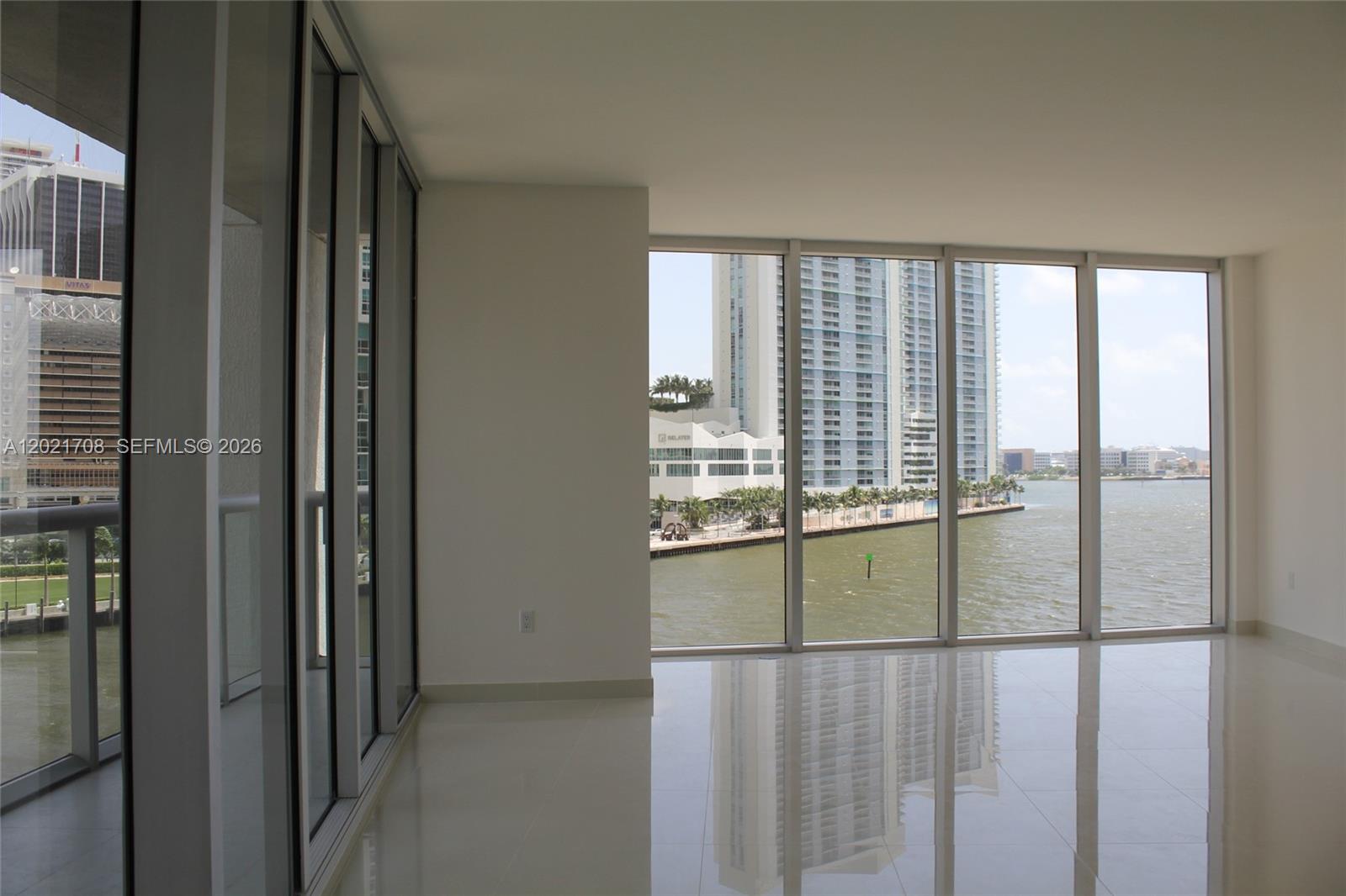 An empty room with white tile floors and floor-to-ceiling windows overlooking a waterfront cityscape — 465 BRICKELL AV # 502, Miami FL 33131, MIAMI, FL