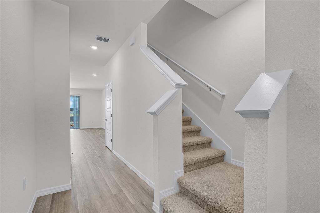 A carpeted staircase with a white railing sits beside a hallway with light wood flooring — 2582 OLYMPIC COURT, DAVENPORT, FL