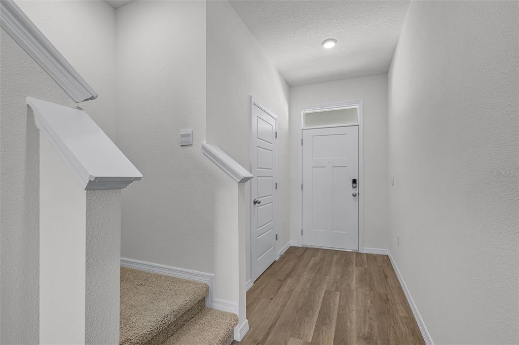 An entryway features wood-look flooring, a white front door, and stairs with beige carpeting — 2582 OLYMPIC COURT, DAVENPORT, FL