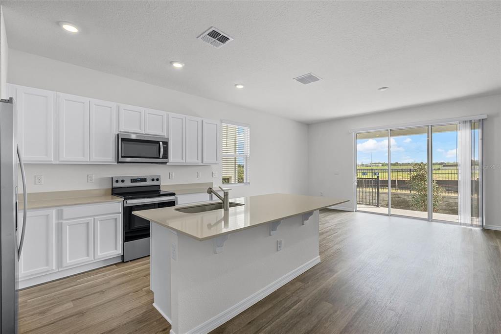 A kitchen with white cabinets, stainless steel appliances, a quartz island, and sliding glass doors — 2582 OLYMPIC COURT, DAVENPORT, FL