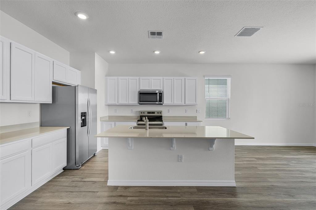 A modern kitchen features white cabinets, stainless steel appliances, a center island, and wood-look flooring — 2582 OLYMPIC COURT, DAVENPORT, FL